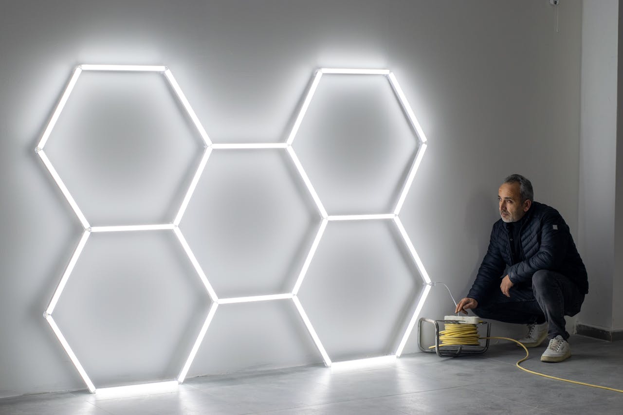 A man installing hexagonal LED light fixtures on a wall, indoors.